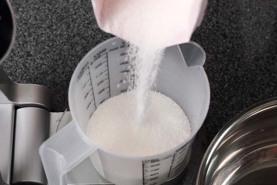 Pouring Sugar into Measuring Cup on Kitchen Scale. Making Golden Syrup Series.