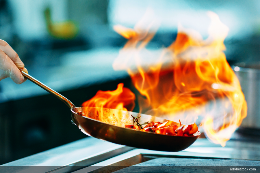 Image of fire in a pan while cooking in a commercial kitchen.