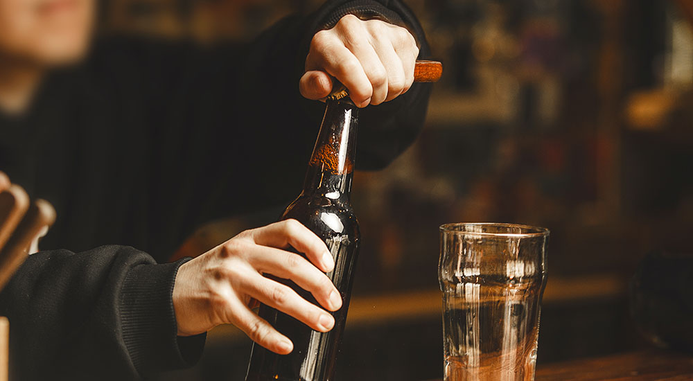Image of bartender opening a bottle of beer on the counter.