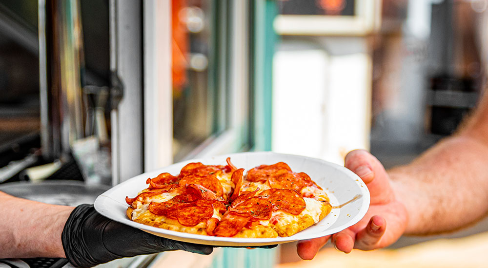 Image of chef handing pizza to customer from food truck.
