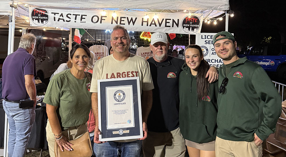 Image of Colin Caplin holding a decree from Guinness World Records marking the world's biggest pizza party.