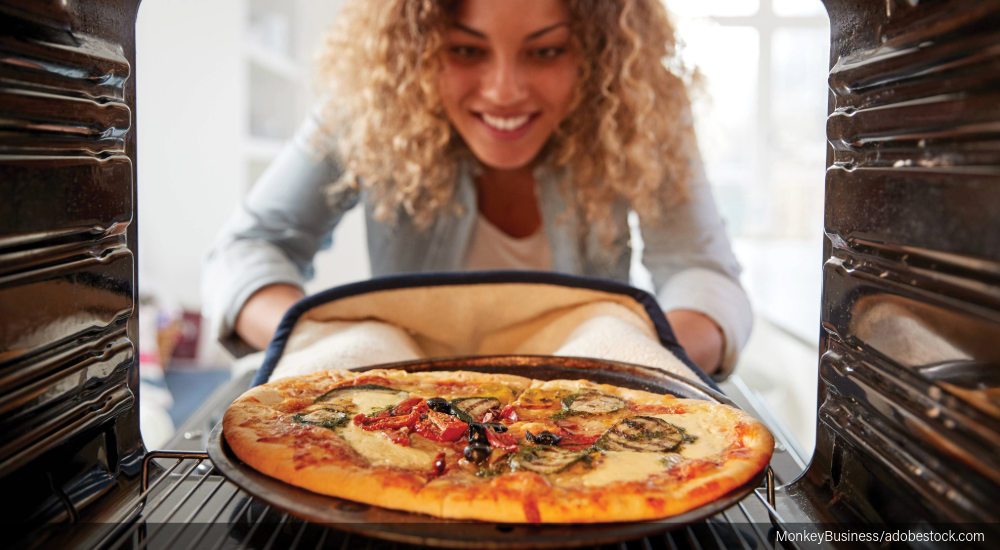 Image of a woman taking a pizza out of the oven.