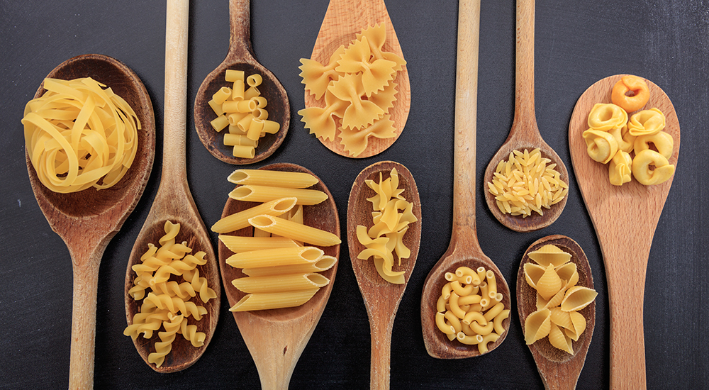 Image of various shapes of pasta on ladles, black background.