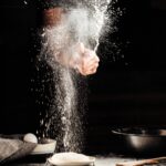 hand dusting flour over pizza dough