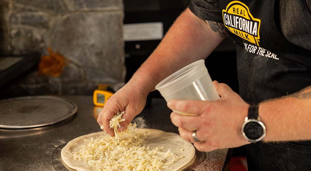 Image of Randy Lewis adding cheese to pizza dough during the 2026 California Pizza Contest.